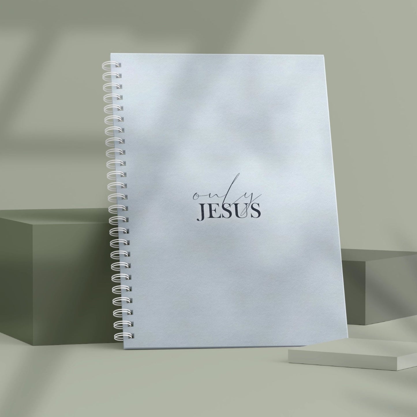 Christliches Notizbuch 'Only Jesus' mit Spiralbindung und schlichtem Design in Blau auf einem Tisch.
